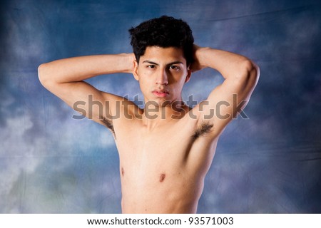 Young, thin Hispanic man standing shirtless with his hands behind his head