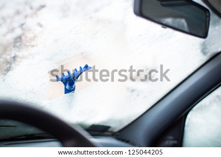 Scrapping frozen car window with blue ice scrapper