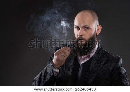 Happy bearded man holding a pipe. It\'s old-fashioned elegantly dressed in a black jacket and vest. Smoke from a pipe around him
