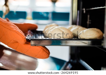 Baker hands with potholder next to metal cookie sheet with bread in oven