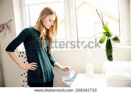 Young blond woman pouring washing powder into the washing machine