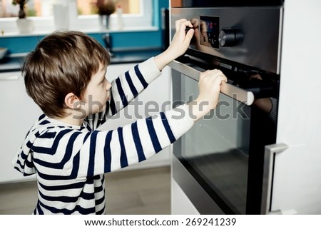Curious little boy dangerously playing with the knobs on the oven. Danger at home