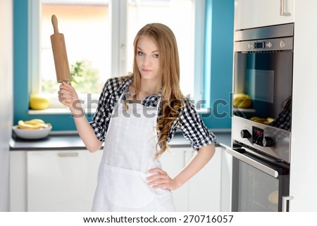 A beautiful young blond woman in a white apron holding a rolling pin