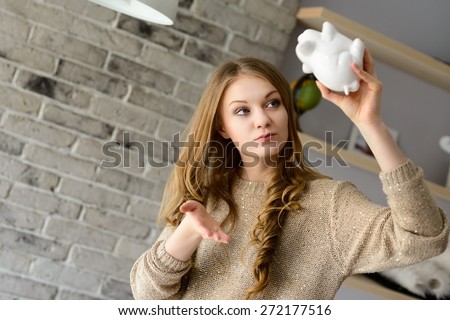 Young blond woman trying to find more money in the piggy bank, lifting it over his head