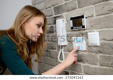 young blond woman activates an alarm in the house. Introduces a code using the keypad