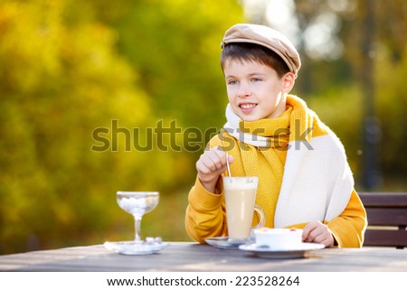 Cute little boy drinking hot chocolate in cafe on beautiful autumn day