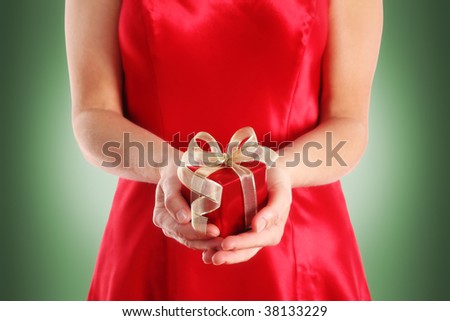 Woman in red dress holding a small red gift box with gold ribbon on green background