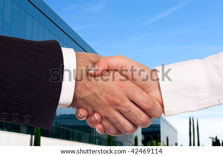 Two hands shaking reaching an agreement with a business building in the background.