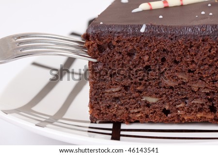 Macro of a piece of chocolate cake with a fork pick up a bit, on a plate against a white background