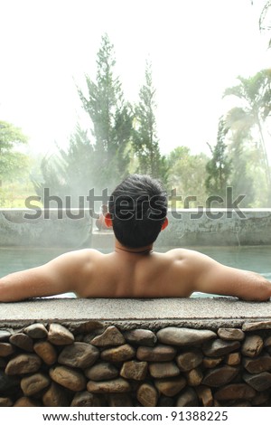 Asian man relaxing in outdoor japanese hot bath.