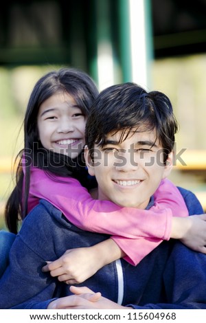Younger sister hugging her big brother around the neck