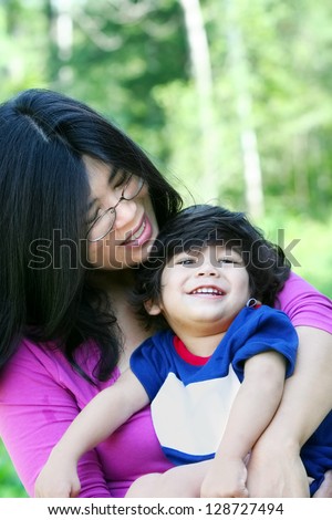 Asian mother lovingly holding her disabled son outdoors in summer. Child is biracial, asian caucasian background.