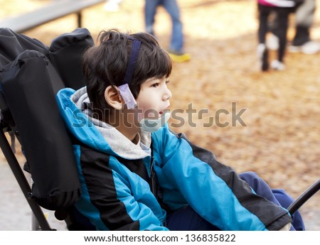 Biracial six year old disabled boy sitting in wheelchair while playing on playground. He has cerebral palsy.