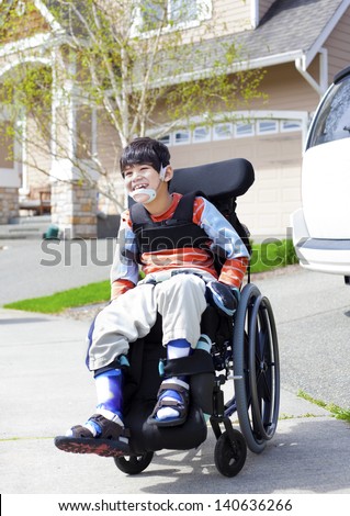 Happy disabled six year old boy waiting on sidewalk in wheelchair. Child has cerebral palsy