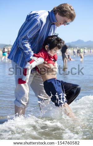 Father helping disabled son walk in the ocean waves on beach. Child has cerebral palsy.