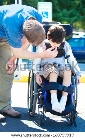 Father helping disabled child in wheelchair. Child has cerebral palsy.
