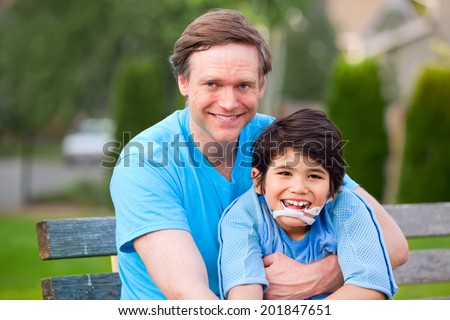 Handsome father sitting with smiling disabled seven year old son outdoors