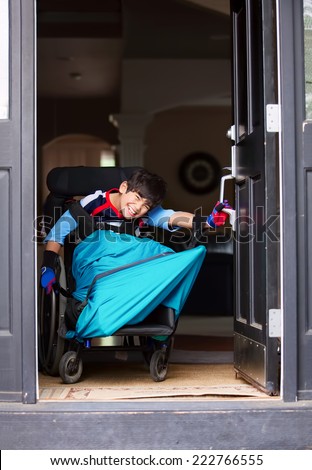 Smiling disabled boy in wheelchair opening front door