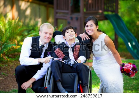 Biracial bride and groom with her little disabled brother in wheelchair on their wedding day