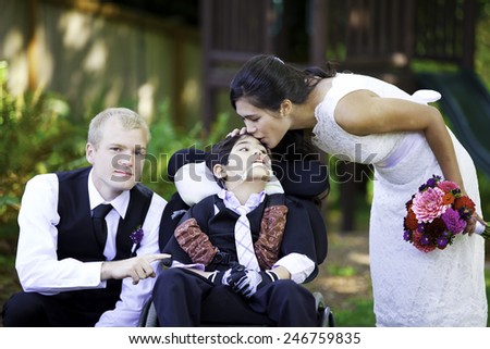Biracial bride kissing her little brother on her wedding day. Child is disabled, in wheelchair