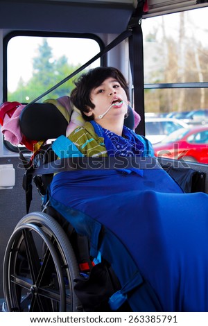 Disabled biracial eight year old boy in wheelchair buckled with seatbelt on school bus