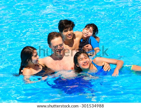 Multiracial family swimming together in pool. Disabled youngest son has cerebral palsy.