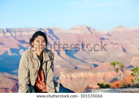 Young biracial  teen girl sitting on rocky edge at Grand Canyon, smiling