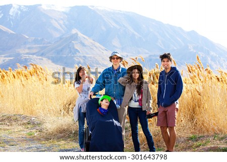 Caucasian father standing by field of tall grasses with biracial children. Youngest child in wheelchair has cerebral palsy.