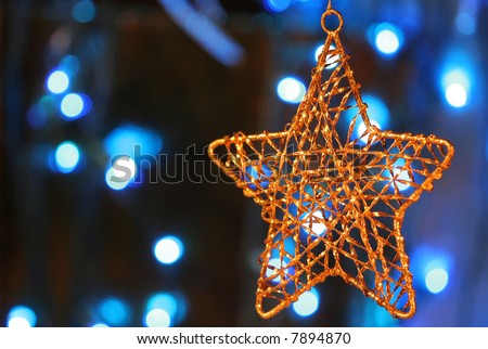 Gold star ornament with Christmas lights in background.