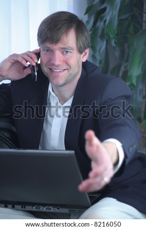 Handsome businessman on laptop and cell phone ready for handshake.
