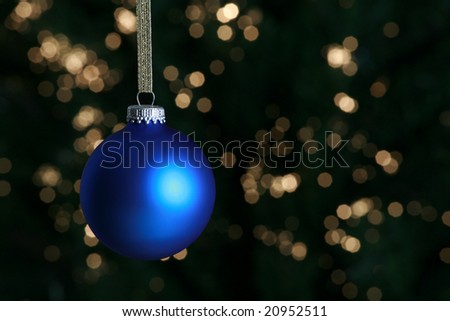 Blue Christmas ornament hanging against lit Christmas tree