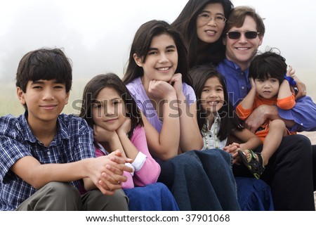Multiracial family sitting on beach on misty, foggy day.
