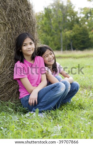 Two young girls sitting against hay bale