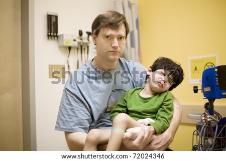 Worried father holding his sick disabled son in doctor\'s office