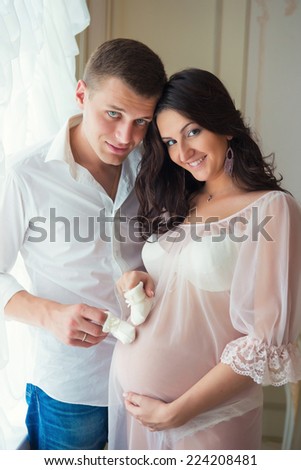 Gentle beautiful pregnant couple near tulle curtains
