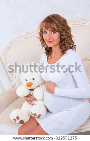 Close-up pregnant girl in knit dress with teddy bear