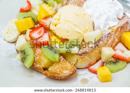 Honey toast with ice cream vanilla, kiwi, mango, banana, apple and strawberry on white plate.