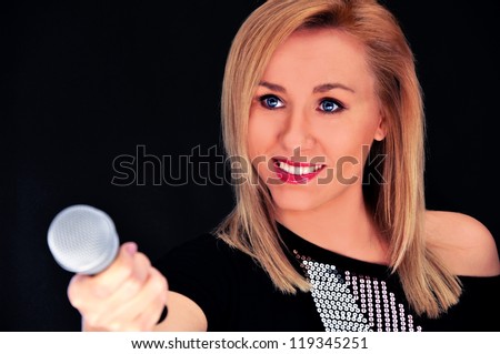 Beautiful blonde woman with microphone on black background