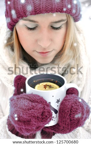 Beautiful blonde woman in winter gloves holding a mug of hot tea outdoor