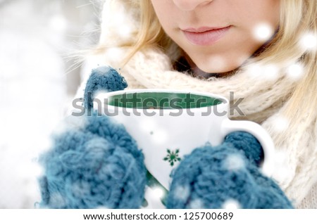 Beautiful blonde woman in winter gloves holding a mug of hot tea outdoor