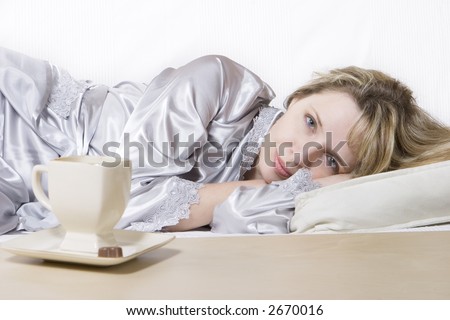 A dreaming women in a silver silk robe relaxing with a cup of coffee on the sofa