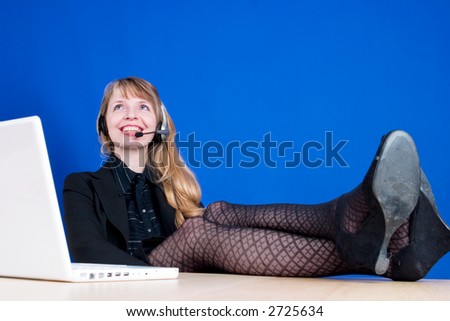 A customer service representative smiling during a telephone conversation with her feet on the desk, shot against a dark blue background