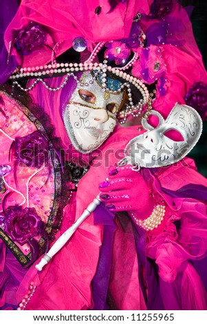 Person holding a silver mask wearing a pink costume at the Venice Carnival