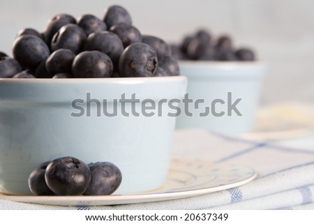 Two dishes of fresh blueberries on a blue and white cloth
