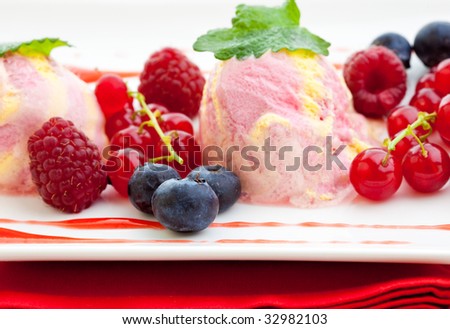 Three scoops of raspberry ice cream with fresh raspberries, red currants and blue berries