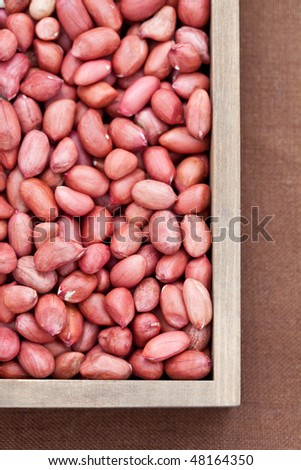 Red peanuts in a wooden box on a brown cloth
