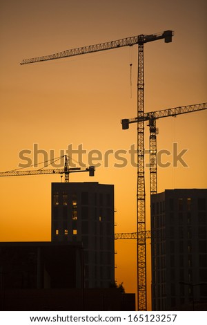 Cranes at sunset. Industrial construction cranes and building silhouettes over sun at sunrise. Vertical format
