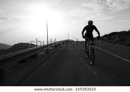 Cyclist man riding mountain on a mountain road, silhouette sunrise.