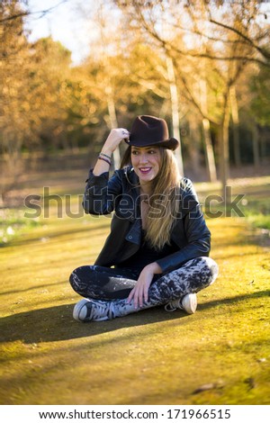 Portrait of a beautiful woman in hat on the park sitting on the floor.