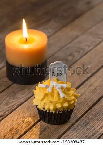 Halloween cupcake with tombstone cake topper and a burning candle on a rustic wooden table